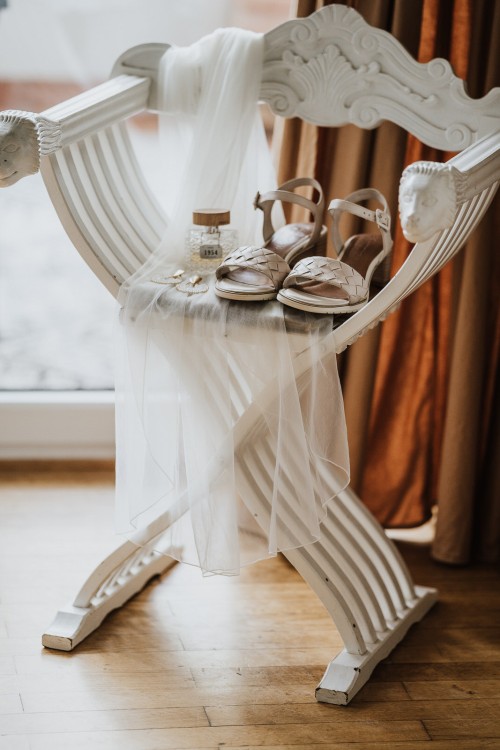 Der Brautschleier, Schuhe und Accessoires liegen auf einem Holzstuhl.