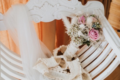 Ein Brautstrauß liegt auf einem Holzstuhl neben einem Schleier.