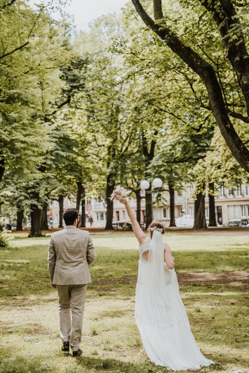Ein Brautpaar läuft durch einen Park und die Braut hält den Brautstrauß hoch.
