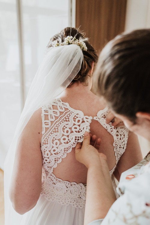 Eine Frau knöpft einer Braut das Brautkleid zu.