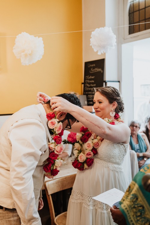 Eine Braut hängt dem Bräutigam einen Blumenkranz um den Hals.