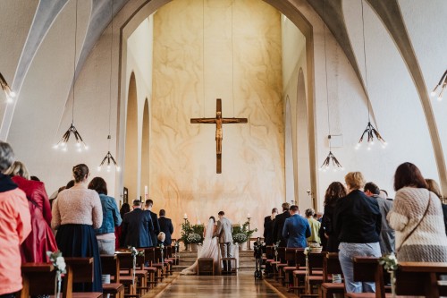 Ein Brautpaar und deren Gäste stehen in der Kirche