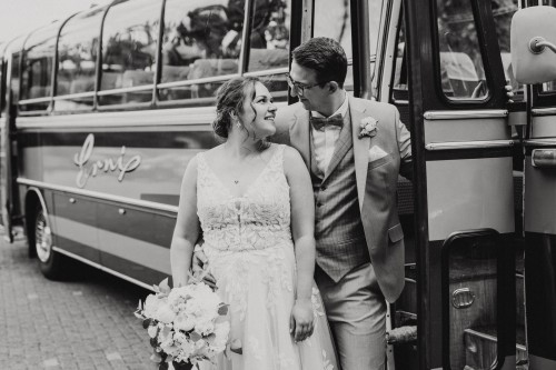 Eine Braut und ein Bräutigam stehen an einem Bus und schauen sich an.