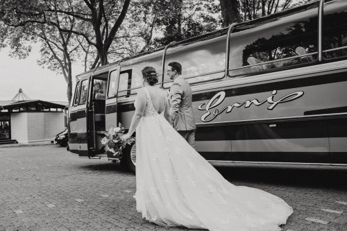 Eine Braut und ein Bräutigam laufen vor einem alten Bus.