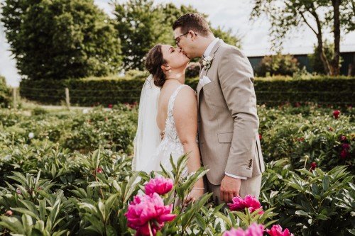 Eine Braut und ein Bräutigam küssen sich im Park zwischen den Blumen.