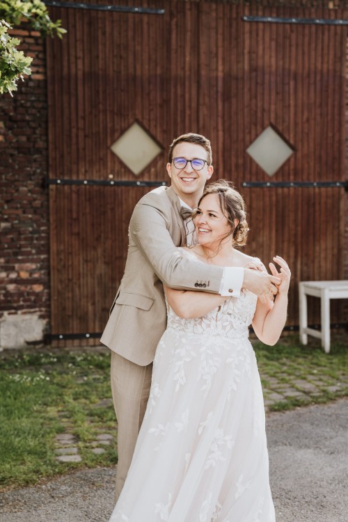 Eine Braut und ein Bräutigam umarmen sich vor einer Scheune.