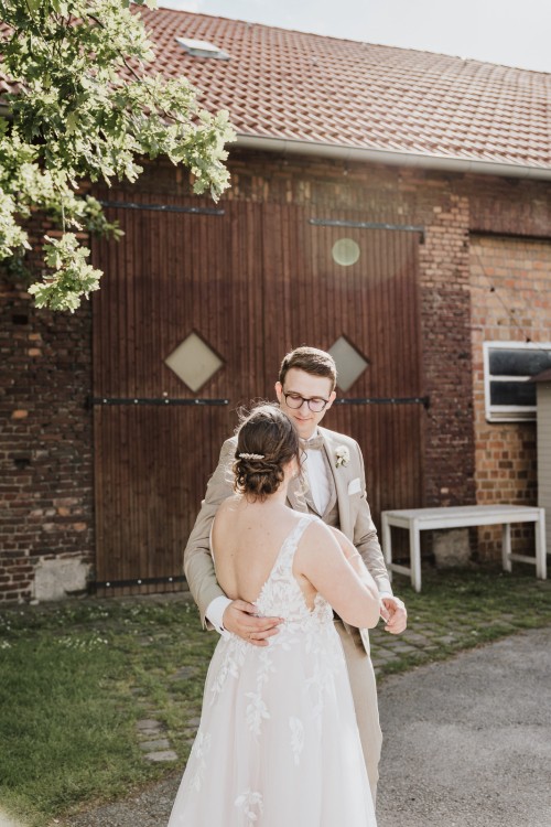 Eine Braut und ein Bräutigam umarmen sich vor einer Scheune.