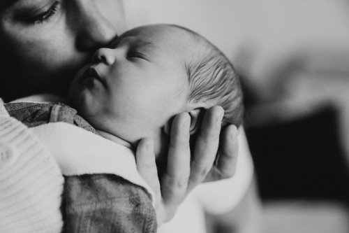 Die Mutter küsst das neugeborenes Baby am Kopf.