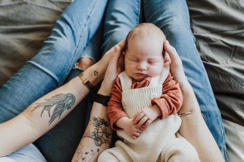 Das Baby liegt auf den tätowieren Händen von ihren Eltern und schläft