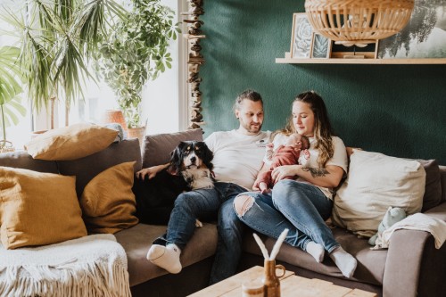 Ein Mann und eine Frau sitzen mit einem Baby und ihrem Hund auf der Couch.