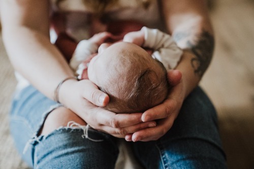 Das Kopf eines Babys festgehalten mit Mamas händen.