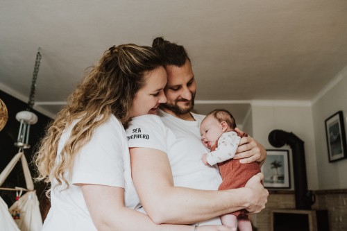 Die jungen Eltern halten ihr neugeborenes Baby fest und schauen es liebevoll an.