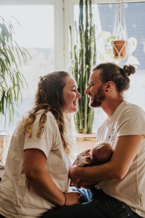 Die jungen Eltern halten das Baby und schauen sich liebevoll an.