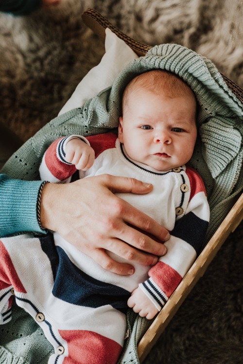 Ein kleines Baby liegt im Bettchen wird von einer erwachsener Hand gehalten