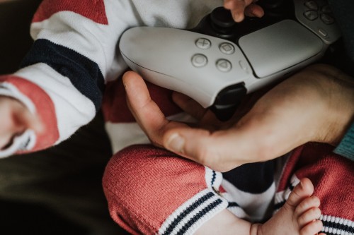Eine Hand die einen Playstation Controller vor dem Baby hält