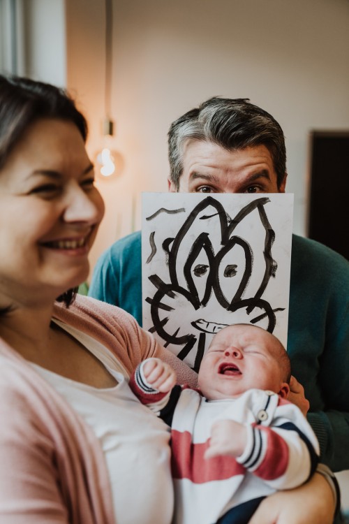 Ein Mann hält eine Zeichnung mit Hasen hoch, eine Frau mit Baby lacht darüber.