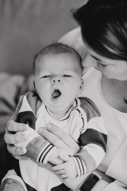 Ein kleines Baby sitzt bei der Mutter am Schoß und gähnt