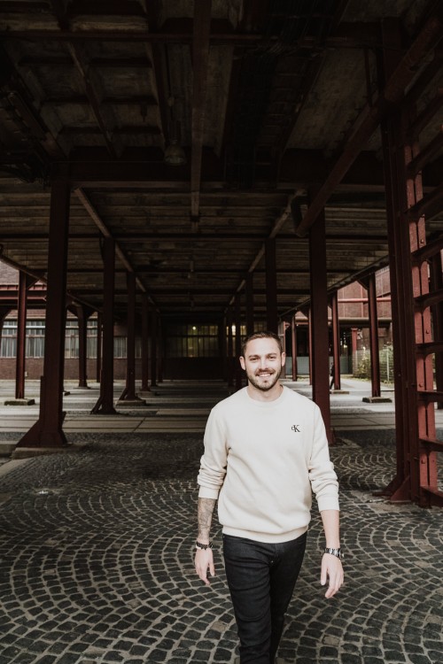 Ein Mann in einem weißen Pullover und einer schwarzen Hose.