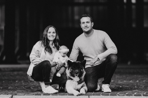 Eine Frau und ein Mann posieren und halten ein Baby und einen Hund in der Mitte.