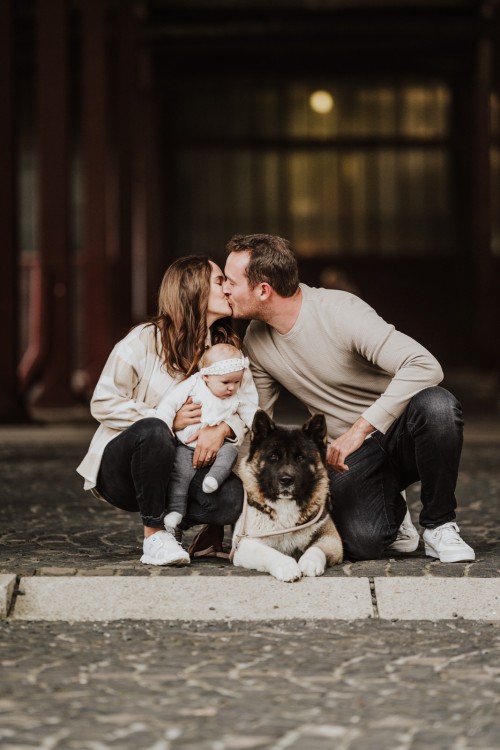 Eine Frau und ein Mann küssen sich und halten ein Baby und einen Hund zwischen den beiden.