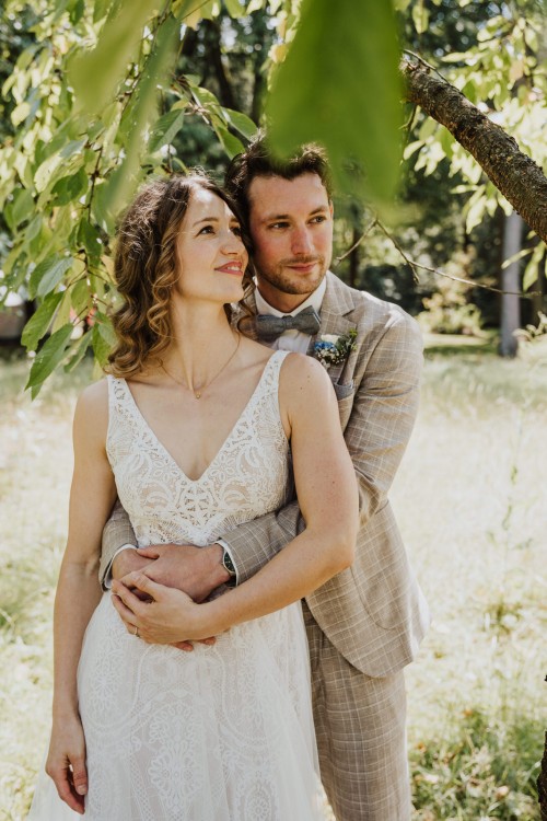 Ein Bräutigam umarmt eine Braut unter einem Baum.