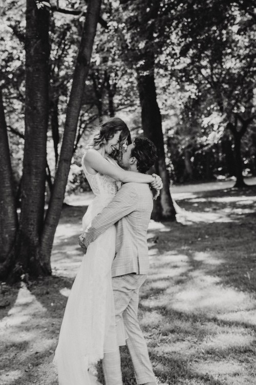 Ein schwarz-weißes Bild von einer Braut die hochgehoben wird von einem Bräutigam.