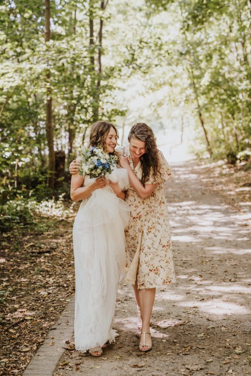Eine Frau umarmt eine Braut mitten im Wald.