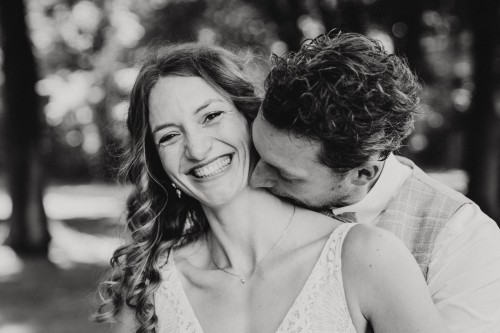 Ein schwarz-weißes Bild von einem Bräutigam der eine Braut am Hals küsst.