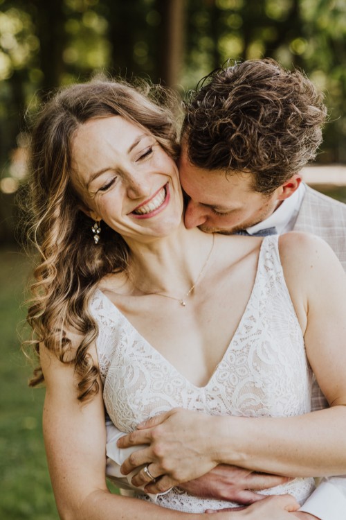 Ein Bräutigam umarmt eine Braut und küsst sie am Hals.