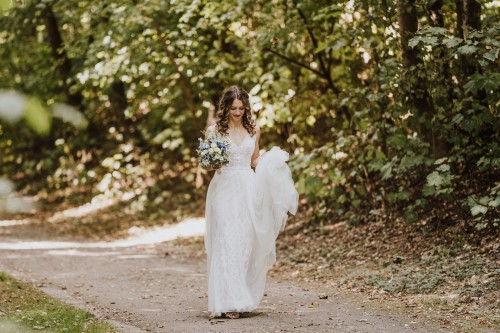Eine Braut geht einem Waldweg entlang.