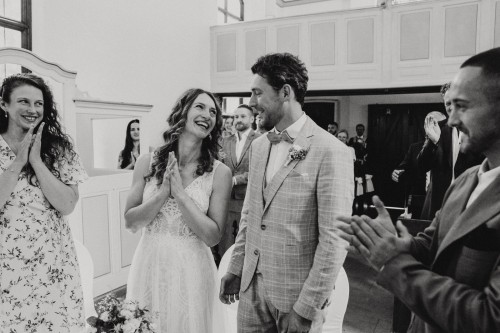 Ein schwarz-weißes Bild von einem klatschenden Brautpaar und deren Gästen.