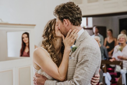 Ein Brautpaar küsst sich und die Gäste schauen im Hintergrund zu.