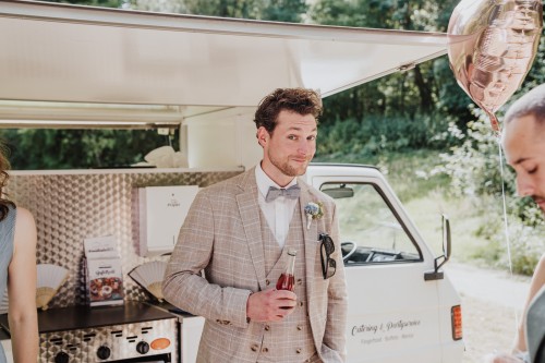 Ein Bräutigam mit einer Flasche vor einem Wagen.