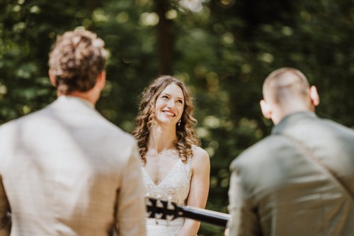 Ein Brautpaar steht im Wald und ein Mann spielt Gitarre.