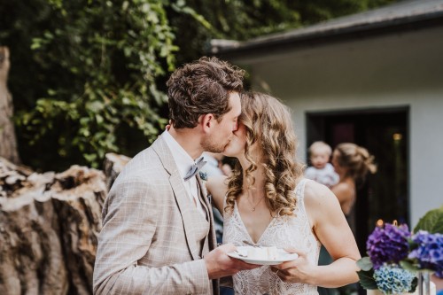 Ein Brautpaar hält einen Teller mit Kuchen und küsst sich.