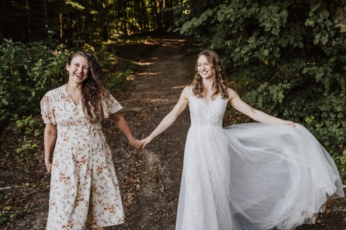 Zwei Frauen halten Händchen und stehen im Wald.