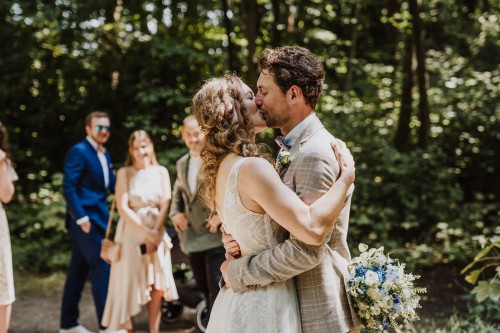 Ein Brautpaar küsst sich und eine Gruppe von Menschen schaut zu.