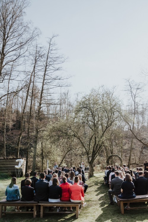 Eine Gruppe von Menschen sitzt vor einem Baum auf Bänken.