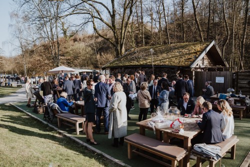 Eine Gruppe von Menschen stehen und sitzen vor einem Haus im Wald.