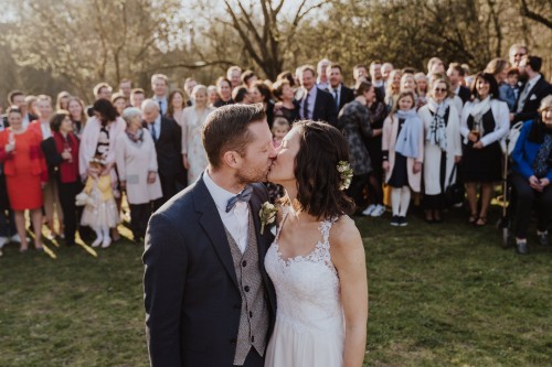 Ein Brautpaar küsst sich und die Gäste im Hintergrund schauen zu.