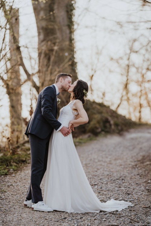 Ein Brautpaar steht auf einem Waldweg und küsst sich.