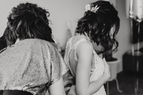 Ein schwarz-weißes Bild von einer Braut der das Brautkleid zugeknöpft wird.