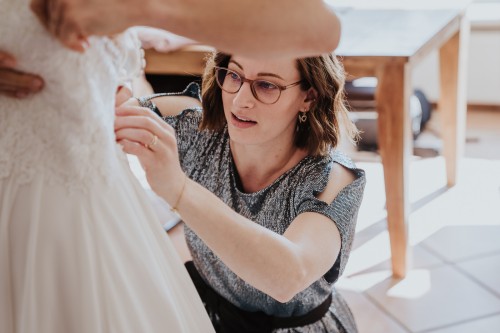 Eine Frau zieht der Braut das Brautkleid an.