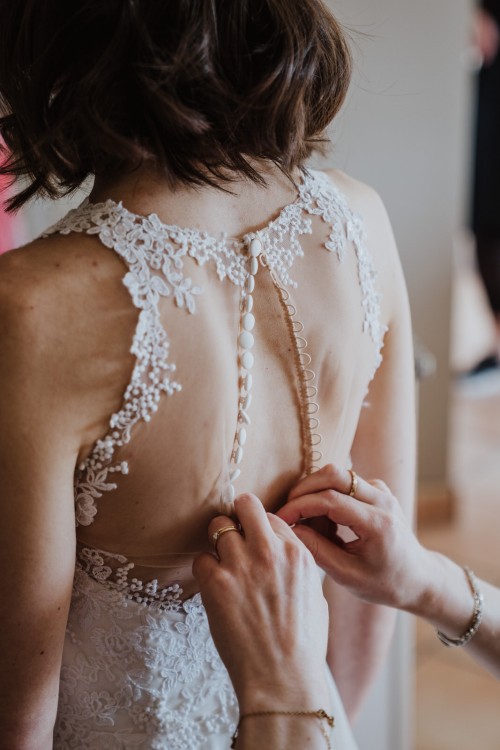 Eine Braut, der das Brautkleid zugeknöpft wird.