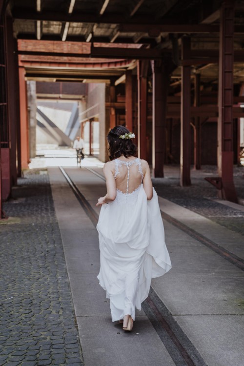 Eine Braut hält ihre Schleppe und geht durch eine Halle.