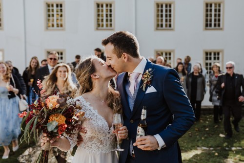 Ein Brautpaar küsst sich und die Gäste im Hintergrund schauen zu.