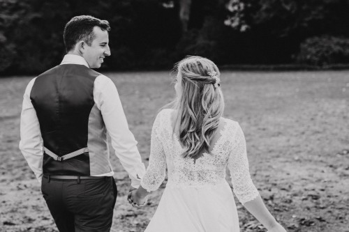 Ein schwarz-weißes Bild von einem Brautpaar, das durch eine Wiese spaziert.