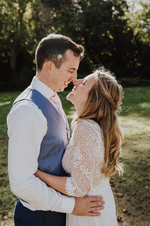 Eine Braut und ein Bräutigam küssen sich auf einer Wiese.