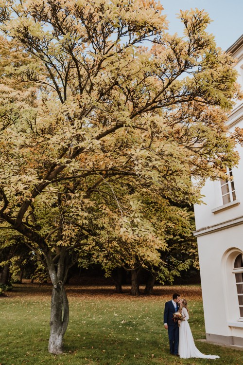 Ein Brautpaar steht unter einem Baum mit herbstlichen Blätter.