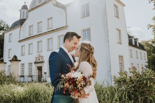 Ein Brautpaar umarmt sich vor dem Schloss Borbeck.